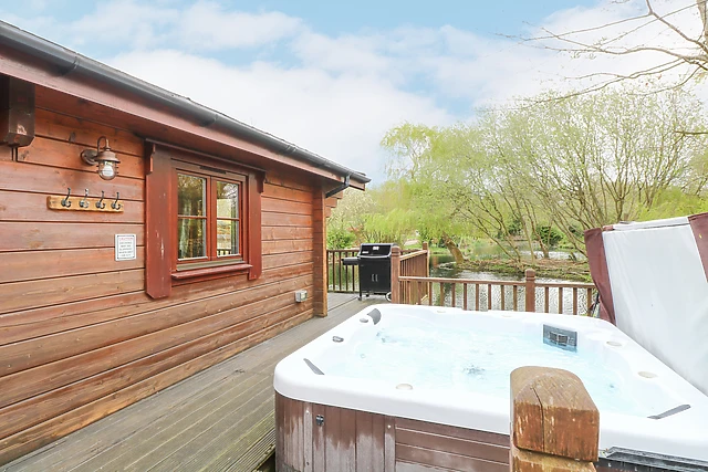 This log cabin lodge in Badwell Ash has its tub on decking right beside the fishing lake